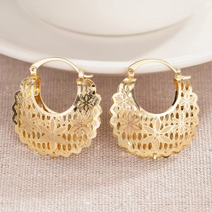 Close-up of golden hollow flower earrings with intricate patterns on a rustic linen fabric