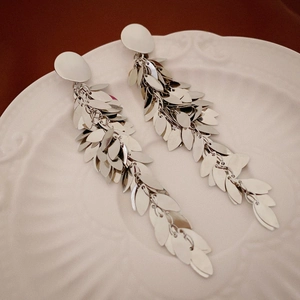 Detail of silver long tassel earrings with metallic leaf sequins on a white ceramic plate