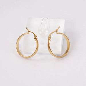 Macro detail of large gold stainless steel hoop earrings on a clear acrylic stand