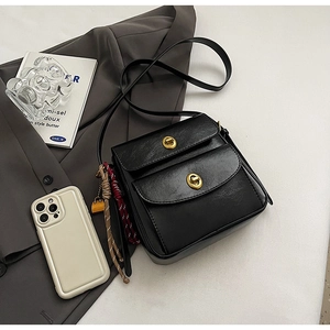 Detail of black crossbody bag with golden oval twist lock and side tassel decoration