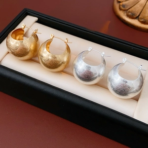 Close-up of thick gold and silver hoop earrings on a black jewelry box cushion