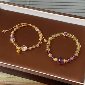 Detail of amethyst and citrine beaded bracelets with a gold bell charm in a tray