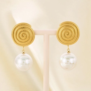 Detailed view of spiral gold drop earrings with large white pearls on a beige display stand