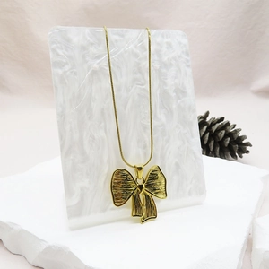 Macro view of golden 18K bow pendant on thin snake chain over marble and stones