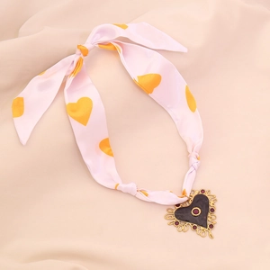 Close-up of a pink silk scarf necklace featuring an ornate vintage heart pendant detail