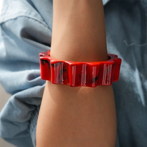 Dettaglio di un bracciale in acrilico rosso a bordi ondulati con trama marmorea
