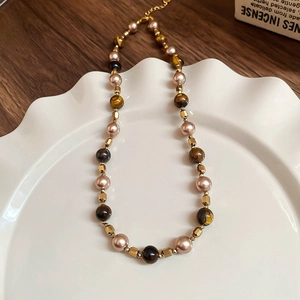 Close-up of tiger eye stone and pearl necklace with golden clasp in a ceramic tray