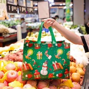Close-up of green Christmas non-woven bag with festive snowman and holiday gift patterns