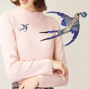 Dettaglio della spilla a rondine con strass blu e cristalli colorati su una maglia rosa