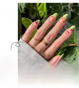 Detail of French green tip press-on nails with red cherry pattern and small rhinestones