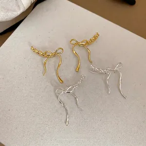 Elegant bow pendant earrings in gold and silver finishes on a minimalist canvas background