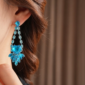 Close-up of elegant long blue crystal heart earrings worn by a model for formal occasions