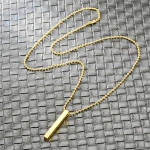 Macro view of gold stainless steel pillar pendant on a bead chain over textured background