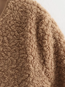 Primo piano del tessuto in pile teddy marrone con texture riccia morbida sulla giacca