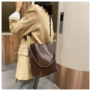Detail of dark brown crocodile pattern bucket bag with shiny texture and gold hardware