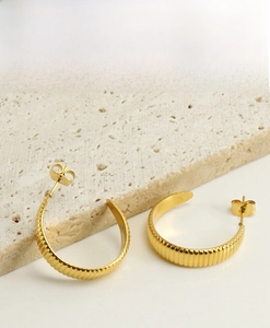 Détail de boucles d'oreilles dorées en forme de C avec rainures sur pierre travertin