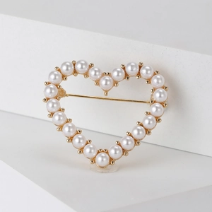 Macro detail of heart-shaped brooch with white pearls on elegant gold metal base