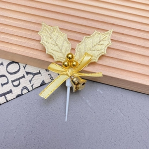 Detailed view of golden holly leaves cake topper with bow and small bell decoration