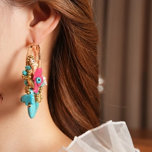 Detail of bohemian earrings with turquoise beads, pink flowers, and seashells on a hoop