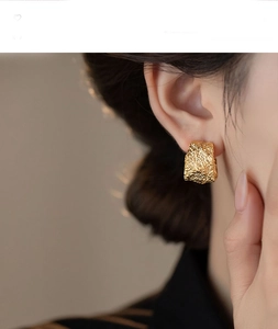 Close-up of golden geometric C-shaped earrings with vintage hammered texture finish