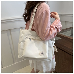 Close-up of white nylon tote bag featuring front zip pocket and good luck patch