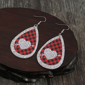 Detail of red buffalo plaid heart earrings with silver glitter on dark wood background