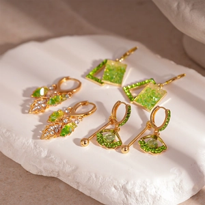 Elegant gold earrings set with green stones and leaf motifs on white marble surface