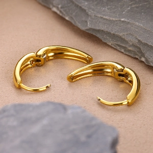 Macro detail of high-polish gold huggie earrings on stone and fabric background