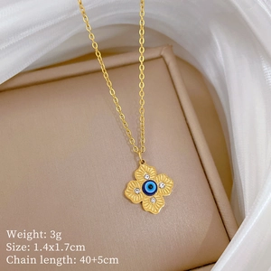 Detail of gold clover necklace with blue evil eye pendant on a beige jewelry case