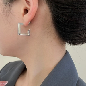 Close-up of a silver geometric twisted earring with a polished finish worn by a model