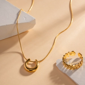 Detail of 18K gold-plated horseshoe necklace and textured leaf ring on stone