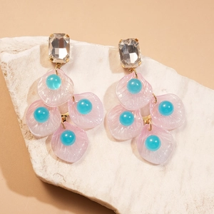 Détail de boucles d'oreilles pétales roses avec perles bleues sur pierre texturée