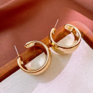 Macro detail of wide gold C-shaped hoop earrings on beige fabric in a wooden tray