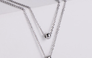 Detail showing a silver double-layer fine chain necklace with polished metal ball pendants