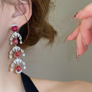 Detail of elegant red heart and water drop tassel earrings worn on a model's ear