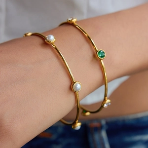 Elegante set di bracciali dorati con perle bianche e gemme verdi al polso