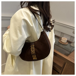 Detail view of brown suede half-moon hobo bag on shoulder showing metal logo