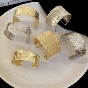 Detail of six minimalist C-shaped metal cuff bracelets with textured patterns in gold and silver