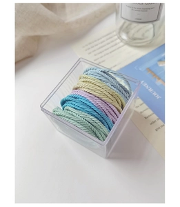 Detail of high-elasticity striped hair ties in pastel colors within a clear storage box