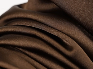 Macro detail of high-shine dark brown satin fabric texture with elegant silky folds
