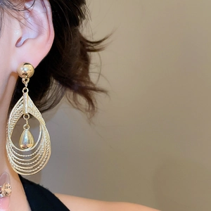 Detailed view of layered hollow teardrop earrings with textured golden finish on model