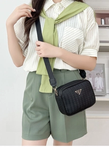 Crossbody camera bag with black woven texture and adjustable strap on fashion model