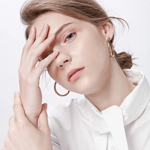 Close-up of model wearing large polished gold stainless steel hollow hoop earrings
