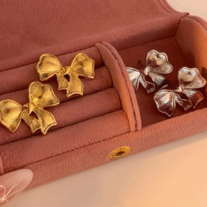 Elegant bow-shaped earrings in gold and silver finish on a pink velvet jewelry box