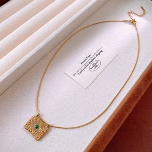 Détail macro du pendentif carré doré avec pierre œil maléfique verte sur présentoir