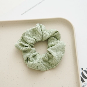 Close-up of light green pleated polyester fabric scrunchie on a beige tray