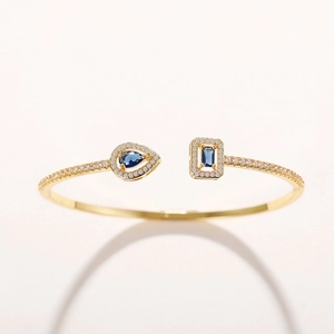 Detail of adjustable gold bangle featuring blue pear and rectangle zircon stones