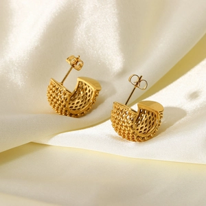 Detailed macro view of 18k gold mesh texture earrings resting on white luxury silk fabric