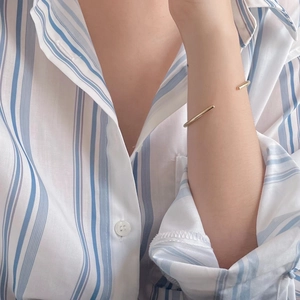 Minimalist gold geometric open bangle bracelet shown on model with striped shirt