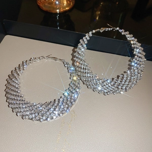 Dettaglio macro dei grandi orecchini a cerchio argentati con design intrecciato e strass